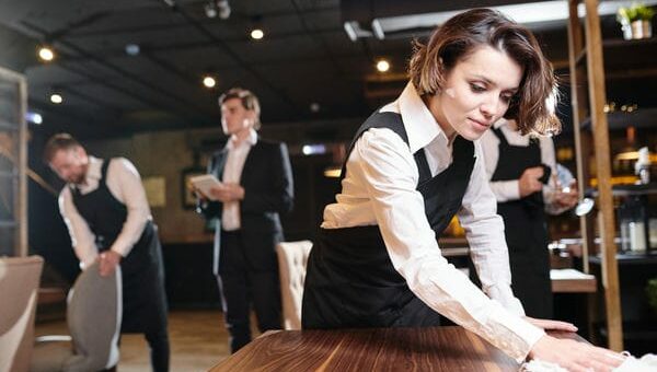 Kellner*in bei der Arbeit. Die Plätze im Restaurant werden gereinigt.