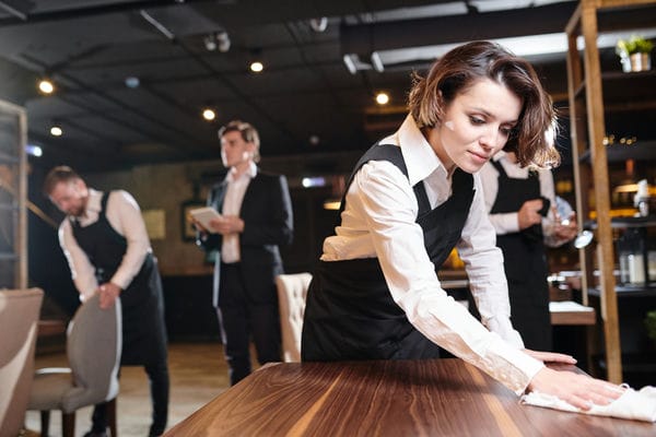 Kellner*in bei der Arbeit. Die Plätze im Restaurant werden gereinigt.