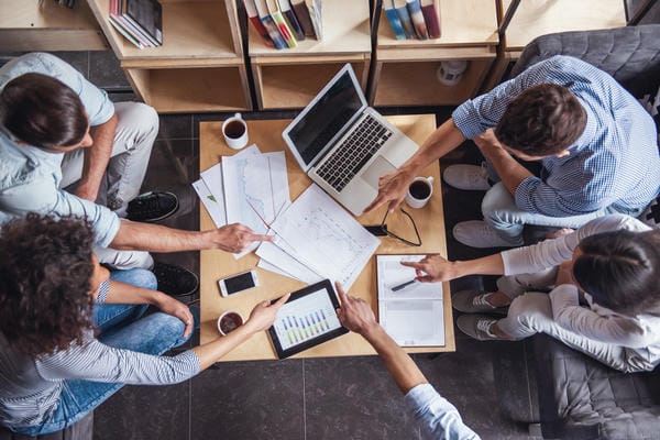 Vier Arbeitskollegen in Gleitzeit arbeiten zusammen an einer Projekt mit Berichten, Tablet und Laptop.