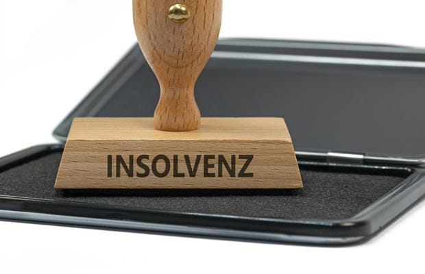 Ein hölzerner Stempel mit dem Aufdruck „INSOLVENZ“ steht auf einem schwarzen Stempelkissen vor weißem Hintergrund.