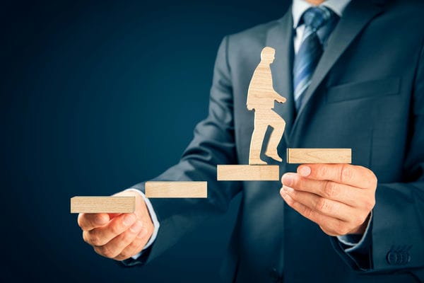 karriere-karrierecoaching Geschäftsmann baut eine Treppe aus Holzblöcken, auf die eine Figur steht