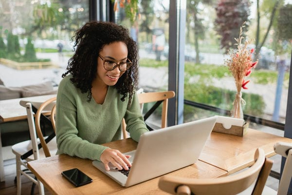 Frau sitzt an einem Tisch und arbeitet an einen Laptop