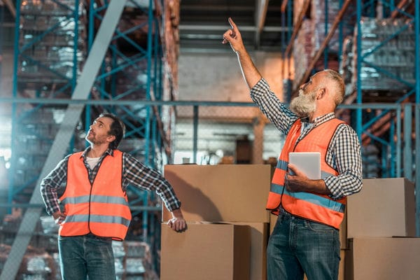 Zwei Mitarbeiter besprechen ihre Aufgaben in einem großen Lager.