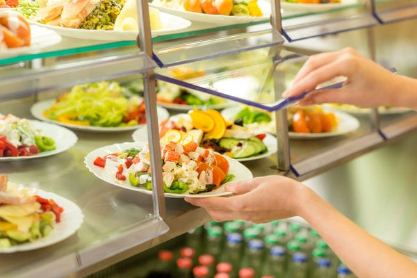 Ein Mitarbeiter bedient sich an der Gemeinschaftsverpflegung und nimmt sich einen Teller Salat.