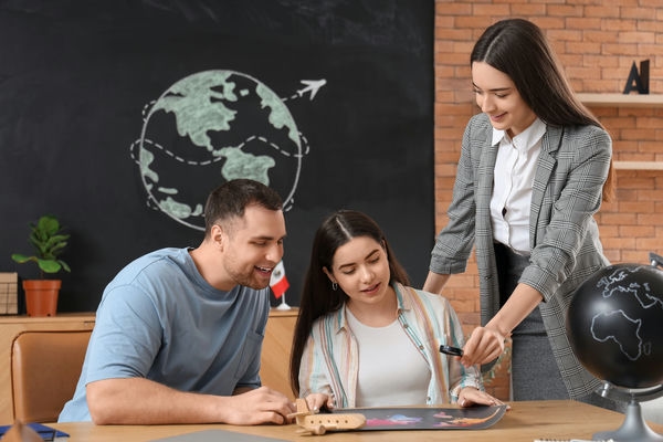 3 junge Menschen, die gemeinsam an etwas arbeiten und sich austauschen im Hintergrund ist ein Globus an die Tafel gezeichnet worden