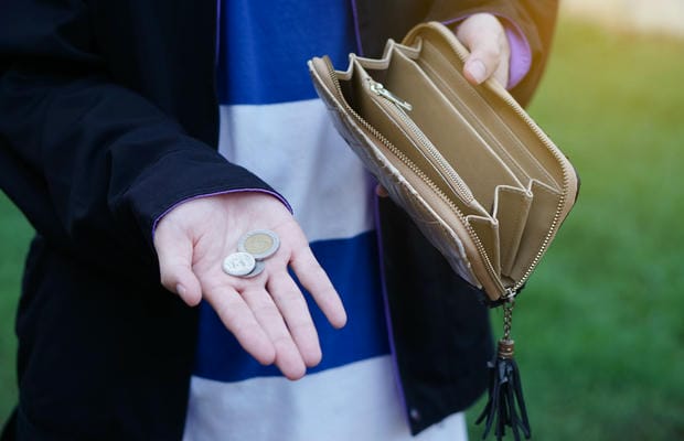 Eine Person blickt enttäuscht auf die wenigen Münzen in ihrer Hand, während das geöffnete Portemonnaie nach Abzug aller Kosten komplett leer ist – ihr bleibt kaum Netto vom Brutto.